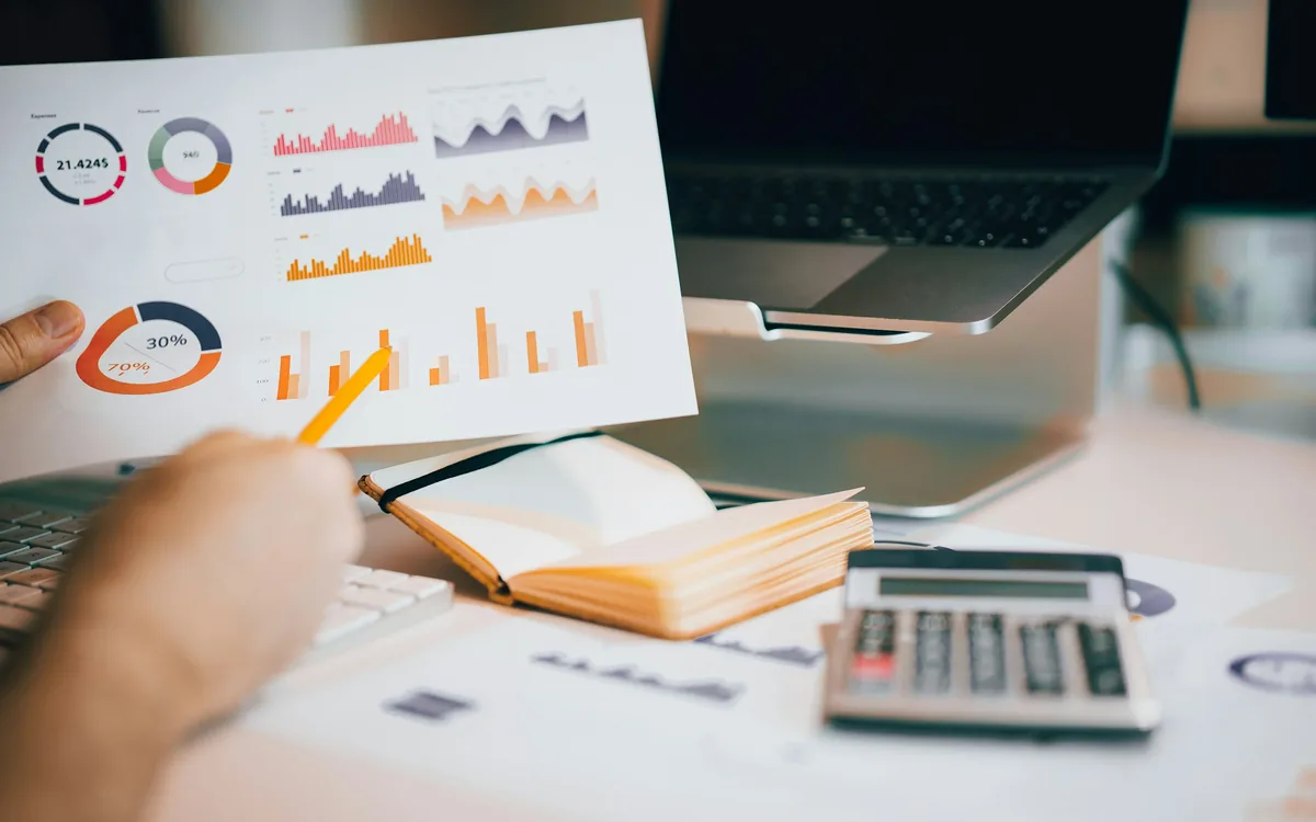 A printed chart held up against a laptop showing the same figures